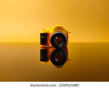 Yellow camera on yellow background with reflection on a black acrylic board