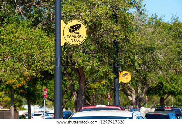 Yellow CAMERAS IN USE signs mounted on metal
light poles at a car parking lot for security purposes to stop auto
theft and crimes.
