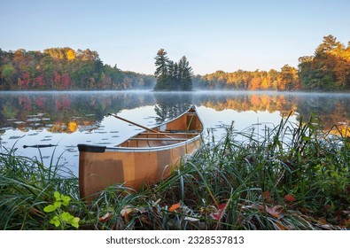 Yellow canoe on shore of calm lake with island and trees in fall color in northern Minnesota - Powered by Shutterstock