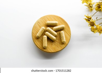 yellow capsules on wooden plate on white background.