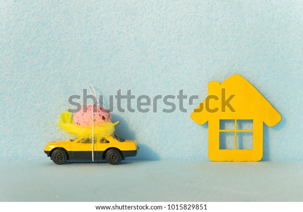 
Yellow car with an egg on the
roof and a house on a blue background. Easter concepts. Holiday for
Easter. Travel to Easter holidays. Travel for the
weekend.