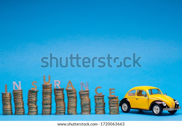 Yellow car figurine next to some tall columns\
of golden coins each with a letter on top together spelling\
insurance, on blue\
background.