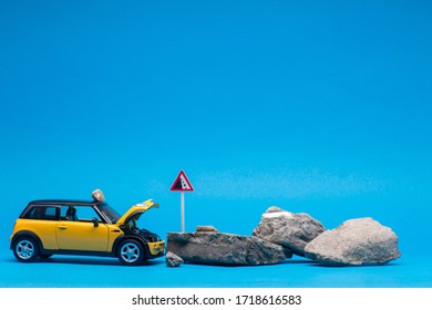 An yellow car with its hood open next to a bunch of stones, on blue background.