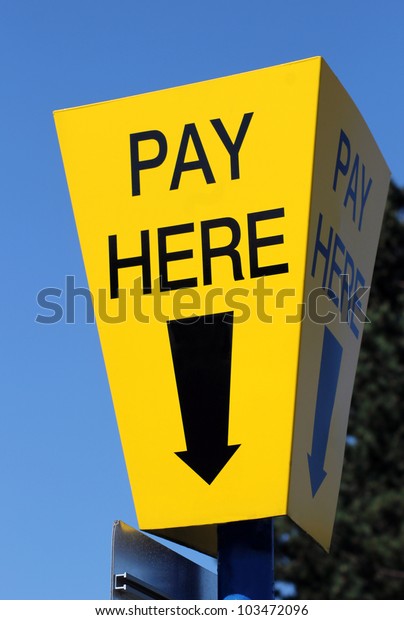 Yellow car parking pay here sign with blue sky\
background and directional\
arrow.
