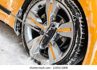 Yellow Car Wheel Washed In Self Service Carwash, Brush Cleaning Aluminium Rim Disc Covered In Shampoo