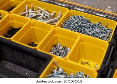 Yellow case with small construction objects. Many storage compartments filled with builders accessories containing screws, nuts, bolts, nails and other tools in workshop. Arranged neatly and organized