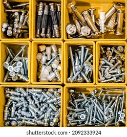 Yellow case with small construction objects. Many storage compartments filled with builders accessories containing screws, nuts, bolts, nails and other tools in workshop. Arranged neatly and organized