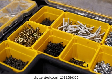 Yellow case with small construction objects. Many storage compartments filled with builders accessories containing screws, nuts, bolts, nails and other tools in workshop. Arranged neatly and organized