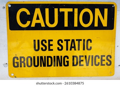 Yellow caution sign instructing the use of static grounding devices for safety purposes