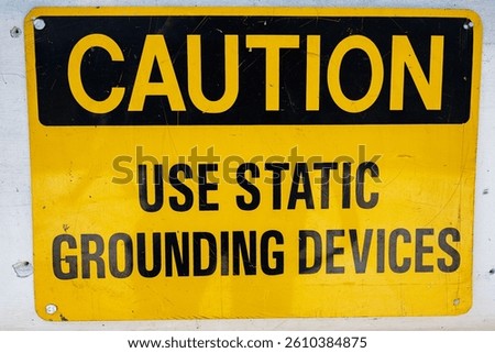 Yellow caution sign instructing the use of static grounding devices for safety purposes