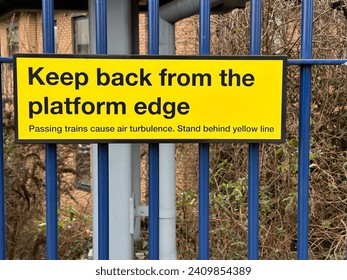 Yellow caution sign keep back from platform edge on a metal fence