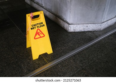 Yellow Caution slippery wet floor sign on the wet ground. Wet floor caution sign on walkway near the building after raining. Warning yellow plastic caution wet floor sign on the ground with copy space