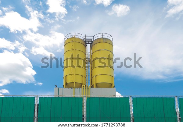 Yellow cement concrete mixing towers with\
safety protection wall and blue sky\
background