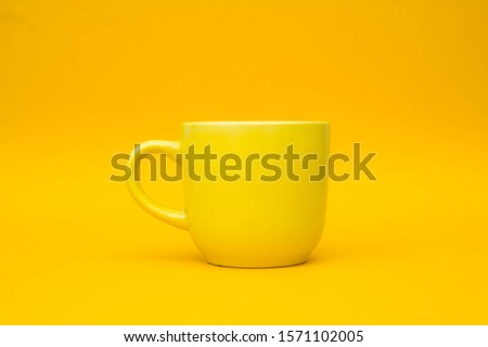 Yellow ceramic cup on yellow background. Yellow mug empty blank for coffee or tea. Space for text
