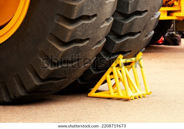 Yellow chock, wheel chock, under\
the wheel of a mining truck. Brake shoe. Security\
engineering.