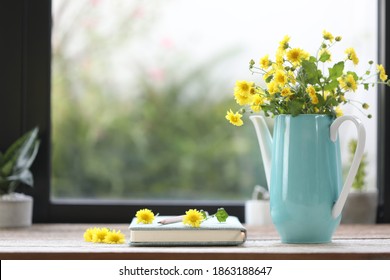 Yellow Chrysanthemum in teal teapot vase with notebook and plant pot in front of windows  - Powered by Shutterstock