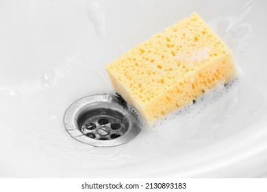 Yellow cleaning sponge with foam in ceramic sink, closeup