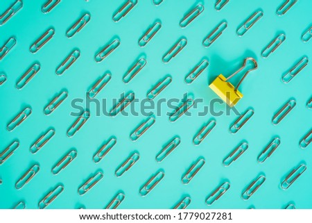 yellow clip laid among pattern of silver paper clip on mint color background , differentiation and outstanding or unique concept
