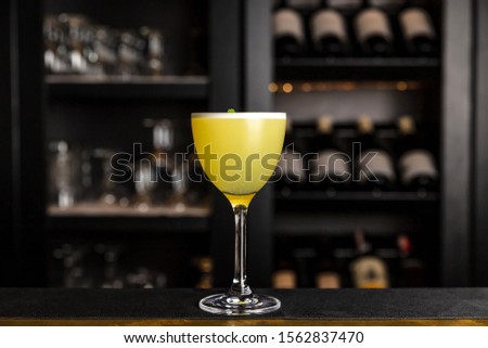 A yellow cocktail in a nick and nora glass garnished with cilantro at the bar