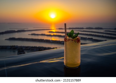 Yellow cocktail on the edge of an infinity pool with a beautiful panorama of the Palm Jumeirah Dubai during sunset - Shutterstock ID 2131157889
