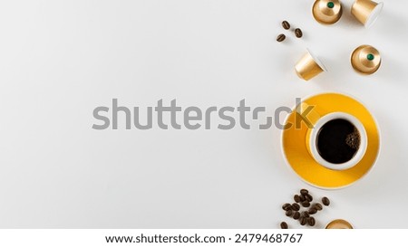 Yellow coffee cup with golden coffee capsules and beans on a white background. Copy space