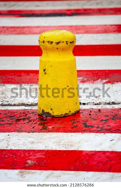 Yellow concrete post on a red and white\
crosswalk. Parking barrier at the zebra\
crossing.