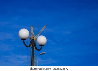 A Yellow Construction Crane Against A Blue Sky Behind A Black Metal Pole And White Street Lights