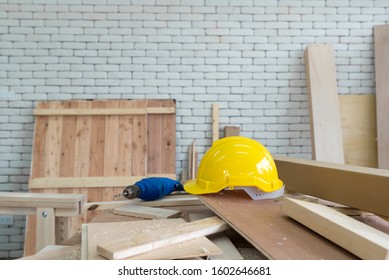 The Yellow Construction Helmet And The Blue Electric Drill Were Left Aside During Lunch Time Brake. A Desk Full Of Hand Tools And Wood Piles. Morning Work Atmosphere In The Workshop Room.