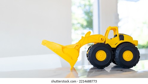 A Yellow Construction Loader Toy Vehicle With Articulated Parts Built With Sturdy Plastic Is Placed On A Table.