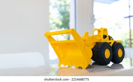 A Yellow Construction Loader Toy Vehicle With Articulated Parts Built With Sturdy Plastic Is Placed On A Table.