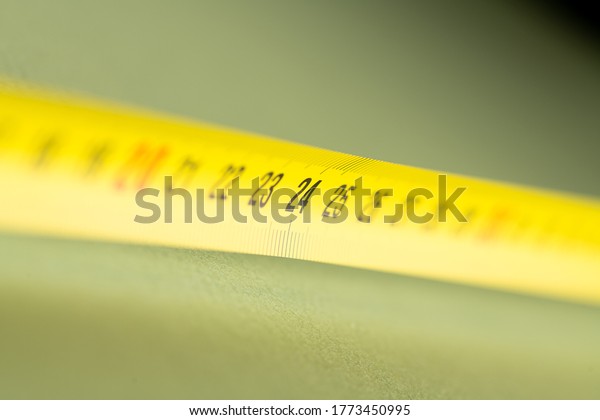 yellow construction measuring tape lies on a table,\
closeup photo in perspective 24 centimeters; green background and\
photo studio light