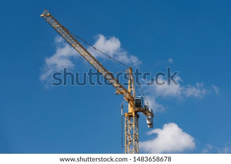 Yellow construction tower crane against blue sky.