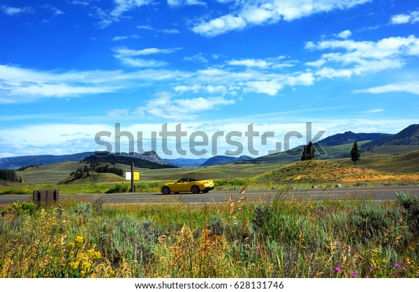 Yellow convertible travels the\
a highway through Lamar Valley in Yellowstone National\
Park.