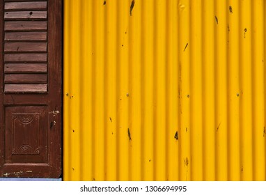 Yellow Corrugated Iron Sheet Wall And Old Brown Wooden Door. Its Can Be Use For 
 Background, Wallpaper Or Backdrop For Photo Studio Fashion Shoot