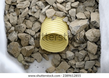 Yellow corrugated pipe with perforation in a trench with crushed stone and geotextile. Drainage works for the removal of ground water in the field.