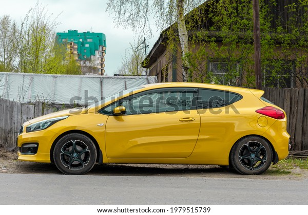 Yellow coupe car against the background of an old
wooden house. Day in city, horizontal shot side view. Surgut,
Russia - 17, May 2021.