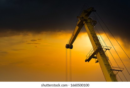 Yellow Crane In Cargo Port Translating Coal. Industrial Scene. Cargo Crane At Sunset