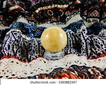 Yellow Crystal Ball, Calcite Crystal Ball On A Variety Of Prints And Lace Fabric Texture Background.