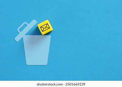 Yellow cube with an email symbol is falling into a blue trash can on a blue background. Depicting deleting emails. Spam mail.