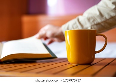 Yellow Cup Of Coffee And A Man Turning A Page In A Book. Reading Concept.