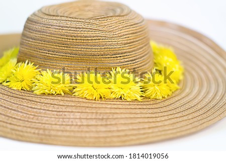 Yellow dandelions lie on a straw hat on a white background. Women's hat with flowers close-up