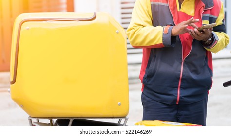 Yellow Delivery Box on Motorcycle with delivery man holding smart phone in front of house.