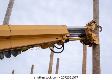 Yellow Digger Truck Arm With Claws Clamped Around Wooden Utility Power Line Pole Against Cloudy Sky With Poles In Background