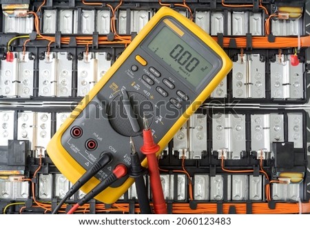 Yellow Digital multimeter with probes on Lithium ion battery background , A multimeter is an electronic measuring instrument, Technology concept