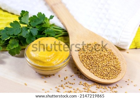 Yellow Dijon mustard sauce in glass dip with wooden spoon full of dry mustard seeds on the table in the kitchen