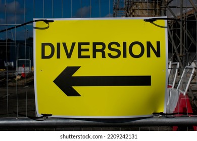 A Yellow Diversion Sign On A Construction Sight Fence