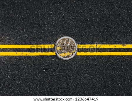 Yellow double solid line with the hatch cover. Road markings on asphalt on the street of Manhattan in New York City. Words NYC sewer on the hatch cover