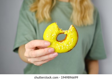 Yellow doughnut with a bitten edge in the hands of a girl. Delicious sweet american dessert. Popular baked goods. Donut in bright sugar glaze close-up. Woman posing with donut in her hands - Powered by Shutterstock