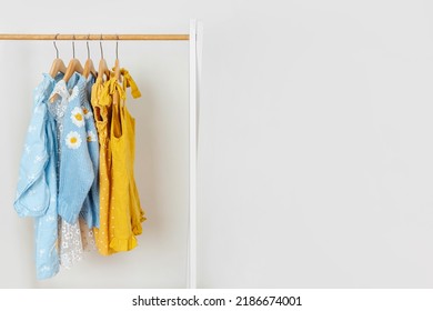 Yellow Dress, Blue Jacket And Sweaters On Hangers In Wardrobe. Wooden Clothing Rack With Children's Outfits. Nursery Storage Ideas. Home Kids Wardrobe. 