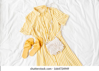 Yellow dress with stripes with  bag and slippers on white bed. Women's stylish  summer outfit. Trendy clothes. Flat lay, top view. - Powered by Shutterstock